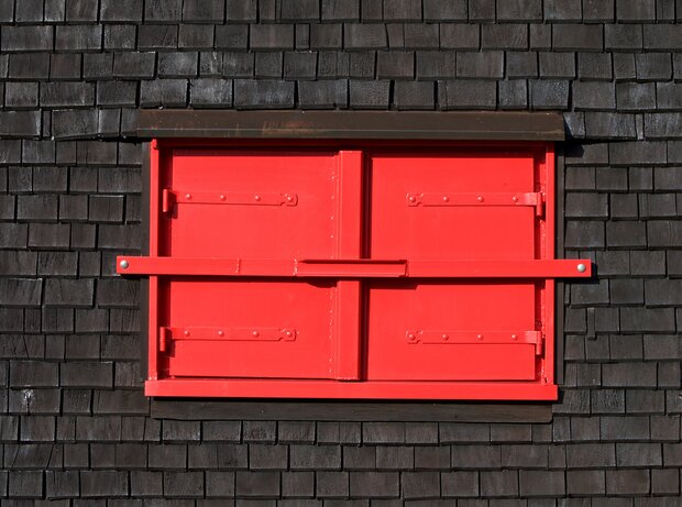 Volets rouges fermés et blocs de ciment en guise de mur.